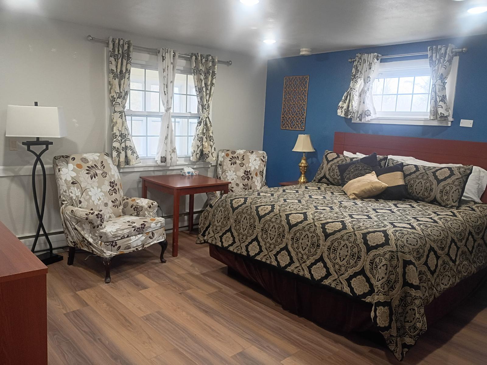 King bed with medallion-pattern bedding, floral wingback chairs and bright windows